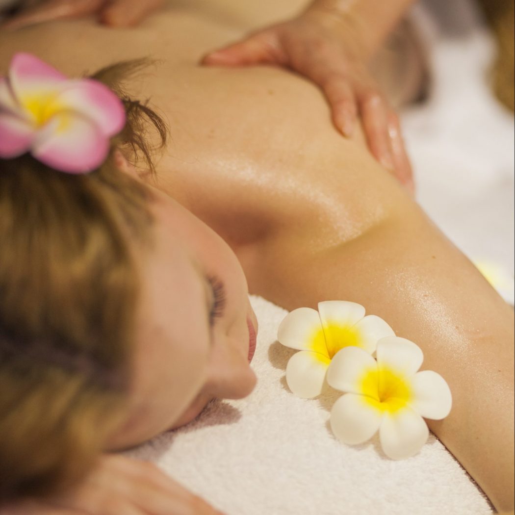 Young female getting massage in Thai massage salon. With some flowers and aromas.